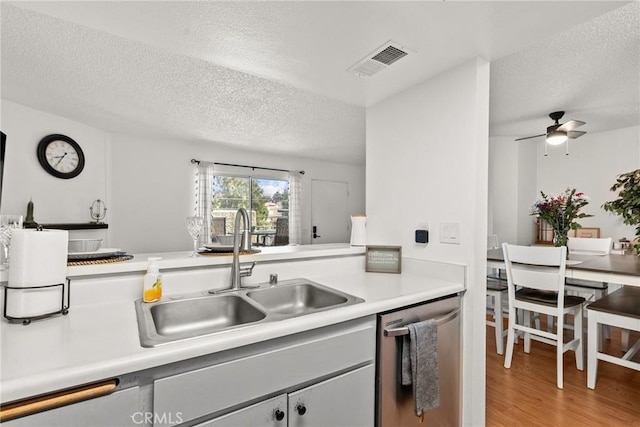 kitchen featuring light wood finished floors, light countertops, visible vents, a sink, and dishwasher