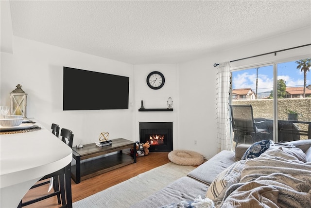 living room with a textured ceiling, a lit fireplace, and wood finished floors