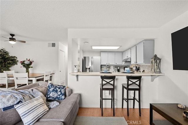 kitchen featuring light countertops, a peninsula, visible vents, and stainless steel fridge with ice dispenser