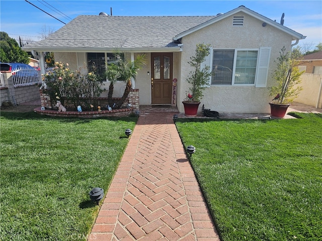 view of front of house featuring roof with shingles, a front lawn, and stucco siding