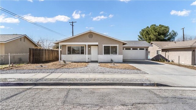 view of front of property featuring a garage, brick siding, fence, driveway, and stucco siding