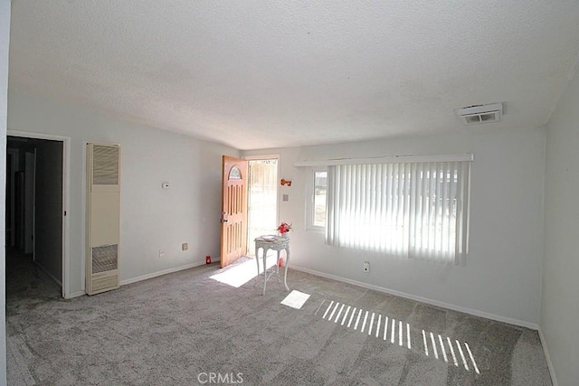 unfurnished room featuring carpet floors, visible vents, a heating unit, and a textured ceiling