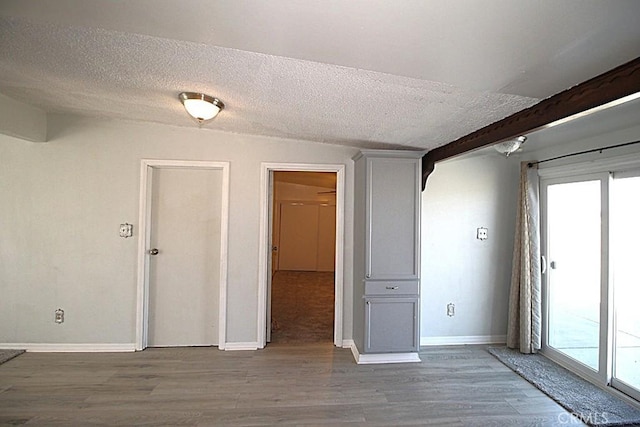 unfurnished room with a textured ceiling, baseboards, wood finished floors, and a healthy amount of sunlight