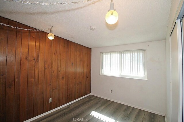 spare room with dark wood-type flooring, wood walls, a textured ceiling, and baseboards