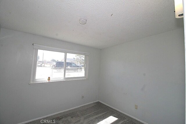 spare room featuring a textured ceiling, dark colored carpet, and baseboards