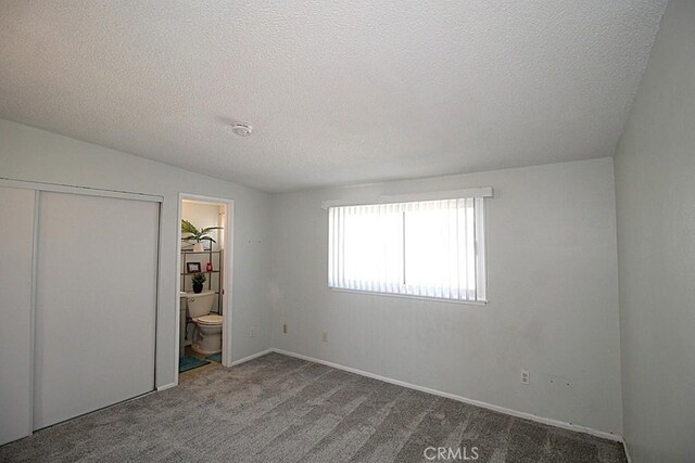 unfurnished bedroom featuring a closet, carpet flooring, a textured ceiling, and ensuite bathroom