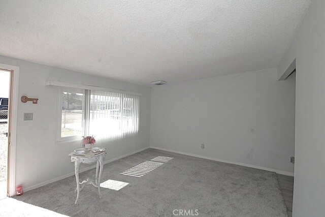 spare room with light carpet, baseboards, and a textured ceiling