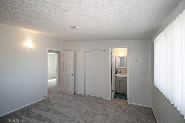 unfurnished bedroom with light carpet, a closet, baseboards, connected bathroom, and a sink