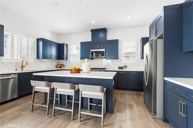 kitchen featuring stainless steel appliances, a sink, a kitchen island, a kitchen breakfast bar, and blue cabinetry