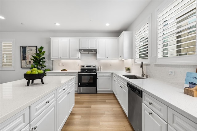 kitchen featuring light wood-style flooring, appliances with stainless steel finishes, white cabinetry, a sink, and under cabinet range hood