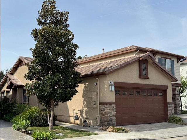 view of front of home with stone siding, a tile roof, driveway, and stucco siding