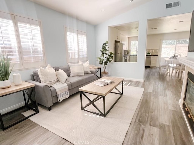 living area with light wood-style floors, visible vents, and vaulted ceiling