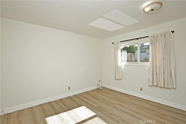 unfurnished room featuring light wood-style floors, a skylight, and baseboards