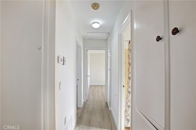 hall with light wood-style floors, attic access, visible vents, and baseboards