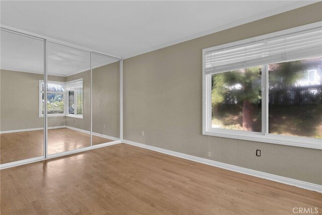 unfurnished bedroom featuring a closet, baseboards, wood finished floors, and ornamental molding