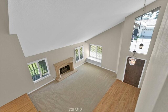 carpeted living area featuring vaulted ceiling, baseboards, a fireplace with raised hearth, and wood finished floors