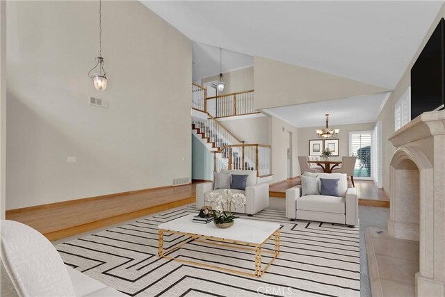 living room featuring a chandelier, high vaulted ceiling, visible vents, stairs, and light wood finished floors