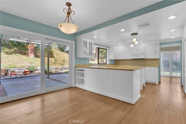 kitchen featuring a peninsula, white microwave, glass insert cabinets, and pendant lighting