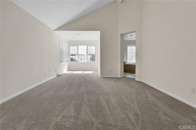 unfurnished living room with carpet floors, high vaulted ceiling, and baseboards