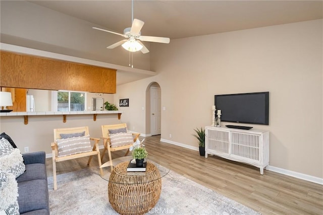 living area featuring baseboards, arched walkways, ceiling fan, vaulted ceiling, and light wood-type flooring