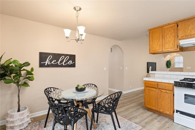 dining area with arched walkways, light wood-type flooring, a chandelier, and baseboards