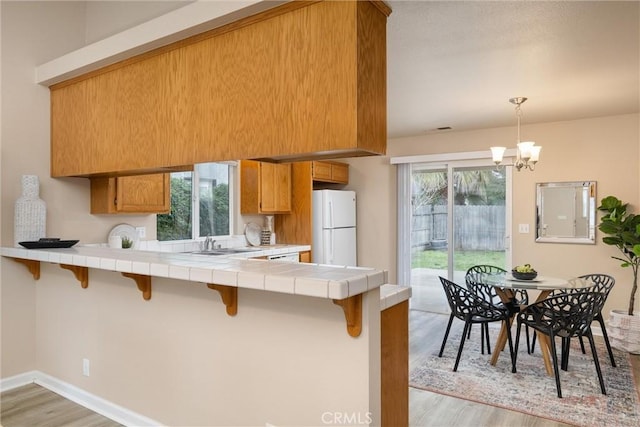 kitchen with brown cabinetry, tile countertops, a kitchen breakfast bar, freestanding refrigerator, and a peninsula