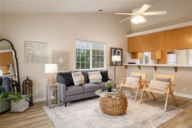 living area featuring a ceiling fan, light wood-type flooring, and baseboards