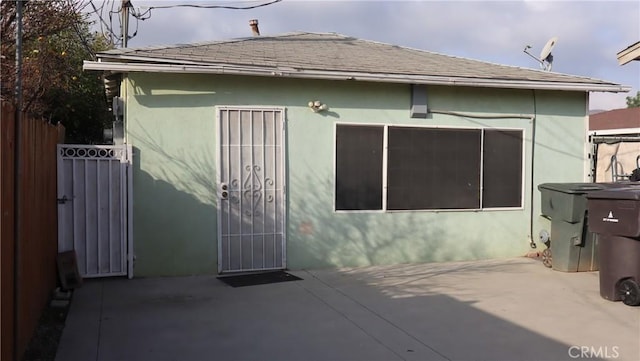 exterior space with a shingled roof, a gate, fence, a patio area, and stucco siding