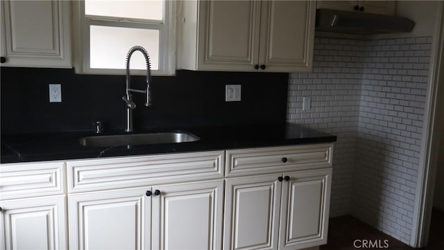 kitchen with dark countertops, tasteful backsplash, white cabinetry, and a sink