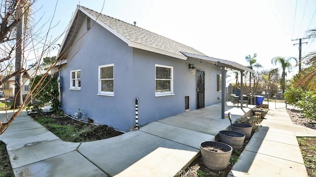 view of home's exterior with a shingled roof, a patio area, and stucco siding