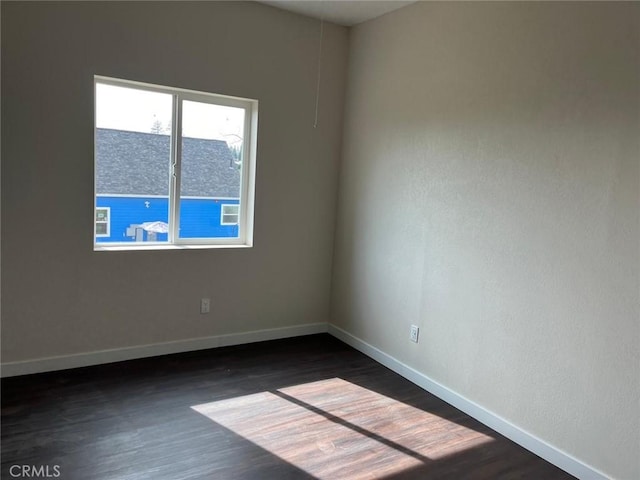 spare room featuring baseboards and dark wood-style floors