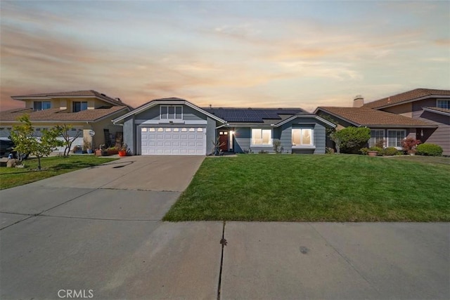 view of front facade with a garage, concrete driveway, solar panels, and a yard