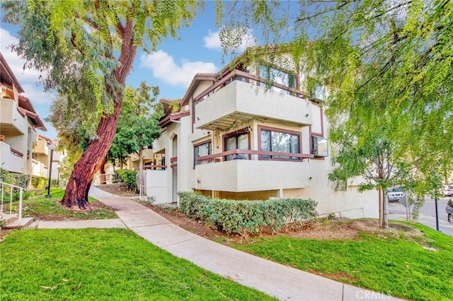 exterior space with a front yard, a balcony, and stucco siding