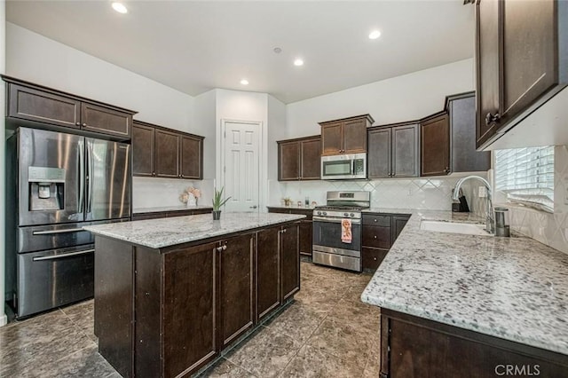 kitchen with light stone counters, stainless steel appliances, a sink, a center island, and decorative backsplash