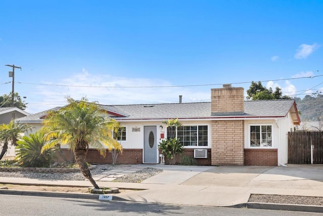 single story home featuring a shingled roof, brick siding, fence, and a chimney