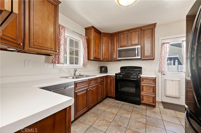 kitchen with a sink, stainless steel microwave, brown cabinets, and black gas range oven