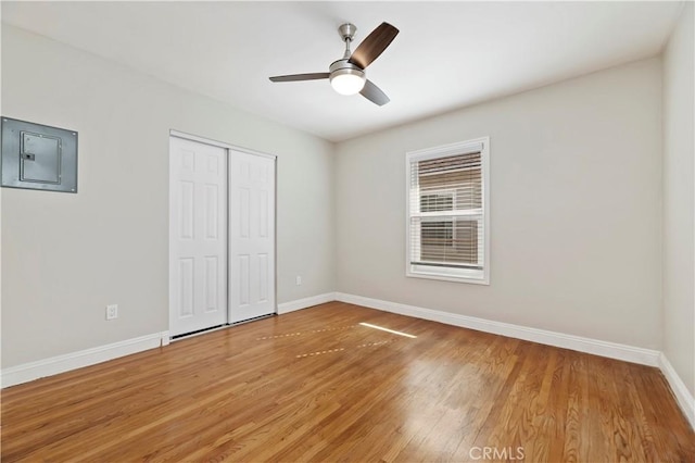 unfurnished bedroom with electric panel, light wood-type flooring, baseboards, and a closet