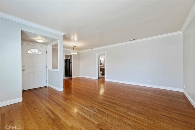 unfurnished living room featuring baseboards, wood finished floors, visible vents, and ornamental molding