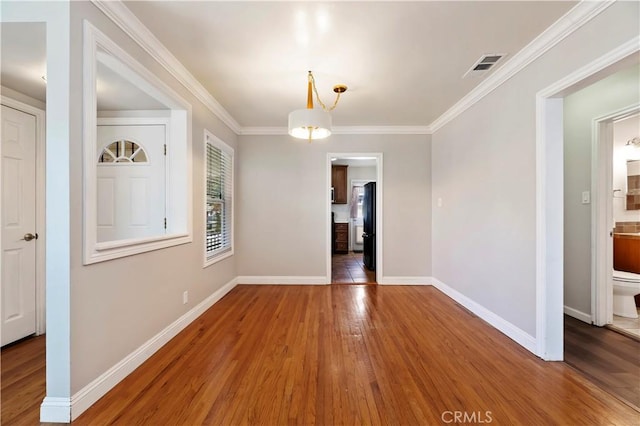 unfurnished room featuring visible vents, baseboards, wood finished floors, and crown molding