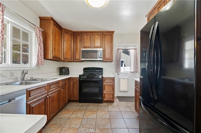 kitchen featuring light countertops, light tile patterned floors, brown cabinets, black appliances, and a sink