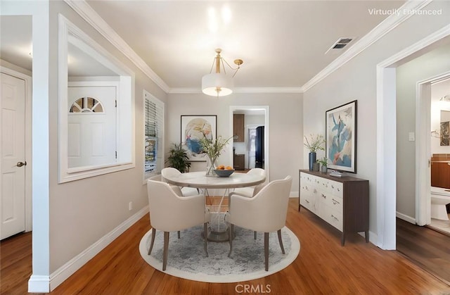 dining room with visible vents, baseboards, wood finished floors, and crown molding