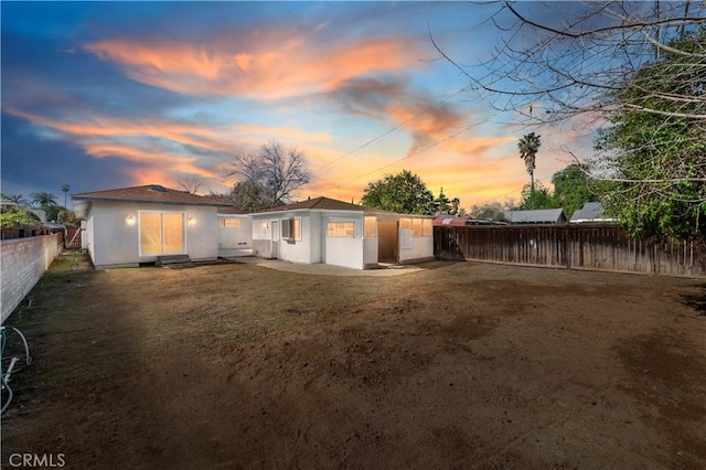 back of property at dusk with stucco siding, entry steps, fence private yard, and a patio