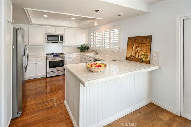 kitchen with white cabinets, tile countertops, a peninsula, a tray ceiling, and stainless steel appliances