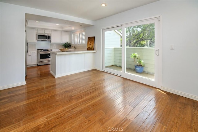 kitchen with light countertops, appliances with stainless steel finishes, white cabinetry, wood finished floors, and a peninsula