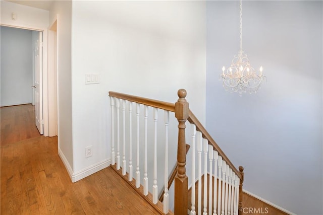 stairs featuring a notable chandelier, baseboards, and wood finished floors