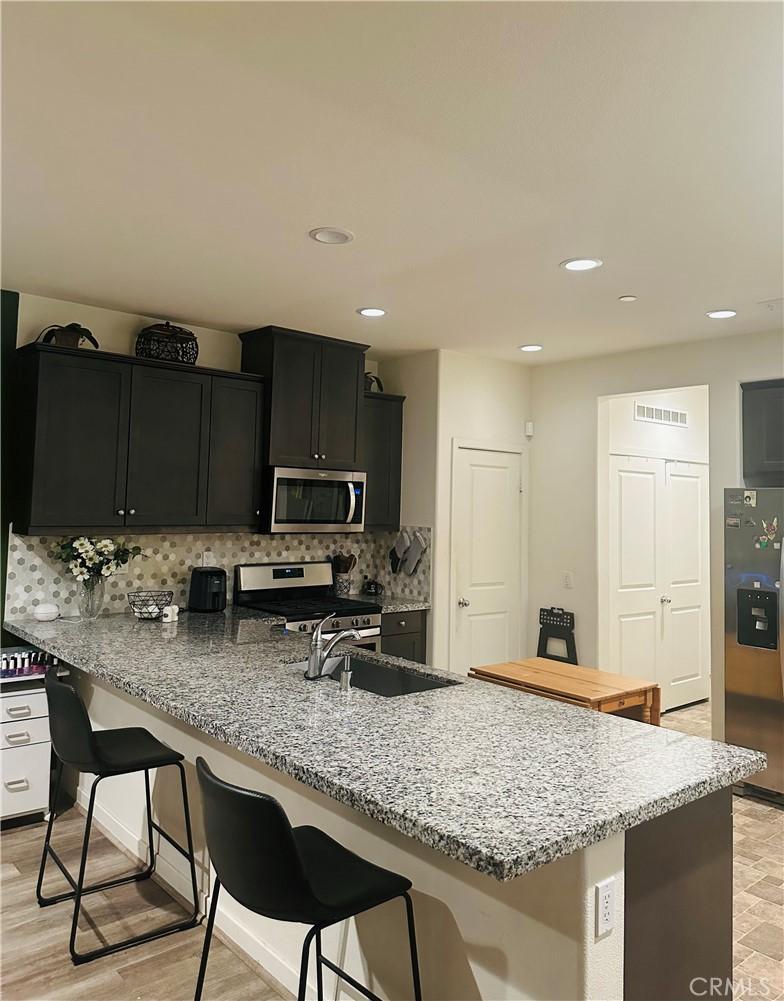 kitchen with light stone counters, a sink, a kitchen breakfast bar, appliances with stainless steel finishes, and decorative backsplash