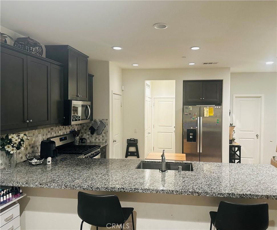 kitchen featuring a sink, visible vents, appliances with stainless steel finishes, light stone countertops, and tasteful backsplash