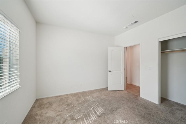 unfurnished bedroom with light colored carpet, a closet, multiple windows, and visible vents