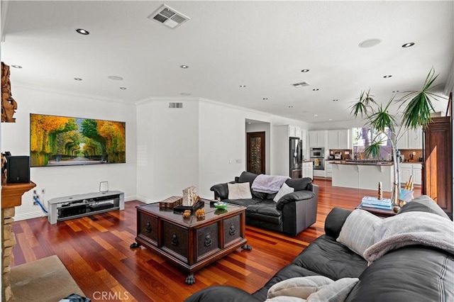 living area with recessed lighting, visible vents, crown molding, and wood finished floors