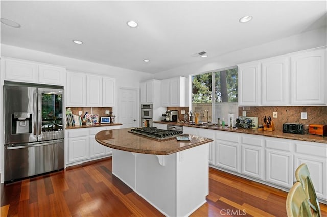 kitchen with dark stone counters, appliances with stainless steel finishes, white cabinets, and a center island